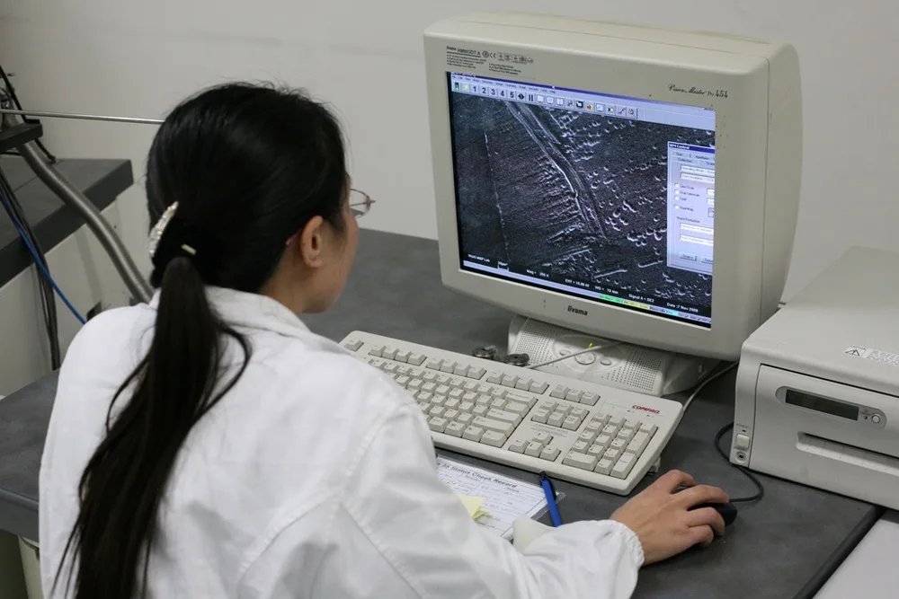 A scientist examines minute details on the surface of a disk drive at a magnification of 100,000 times. The image was produced using an electron microscope.
